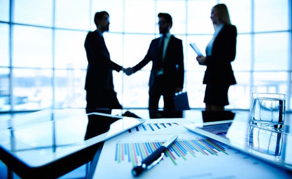 A business meeting between three people with two of them shaking hands.