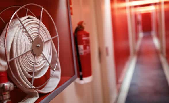 A fire extinguisher and a hose in a corridor.