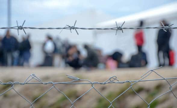 Barbed wire in the camera focus with people in the background who cannot be seen properly.