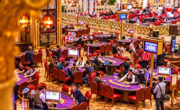 Many gamblers sitting at tables in a Macau casino and playing blackjack.