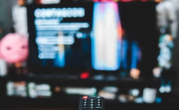 A remote controller pointed at a blurred TV.