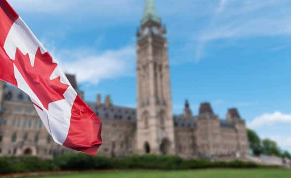 The Canadian national flag flying in the corner of the photo with a blurred building in the backdrop.