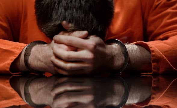 A convict in orange uniform holding his head down in a state of surender, distress or surrender.