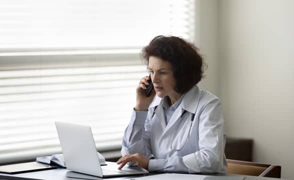 Doctor on call with a patient while using a laptop