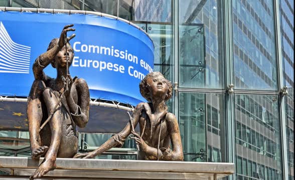 The European Commission as seen from outside with the statues in focus and the blue sign behind.