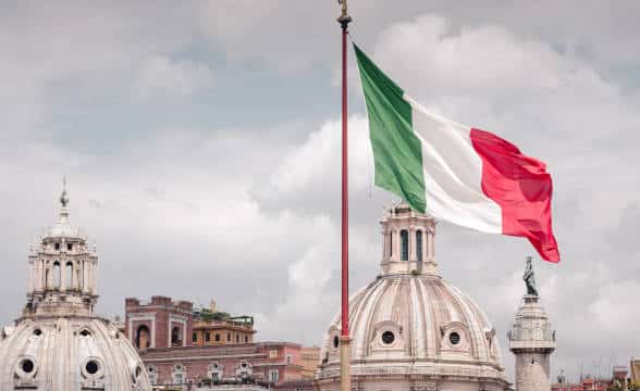 Italian national flag flying above the buildings and city.