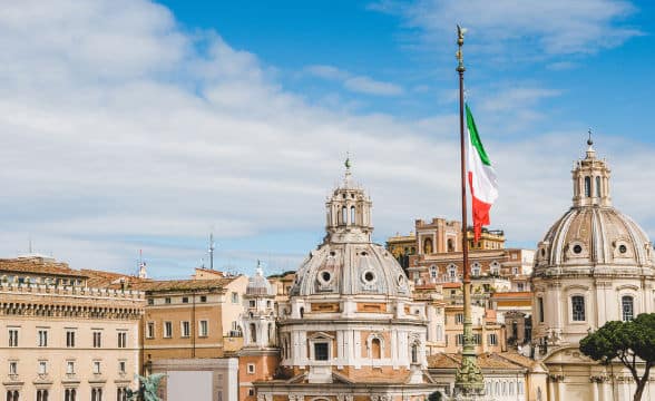 The top of a church in Italy with the Italian flag flying in front of it on a pole.