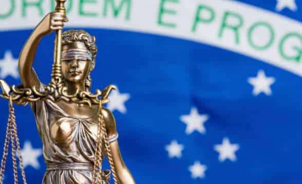 Lady Justice blindfolded and weighing the scales in front of the Brazilian national flag as her background.