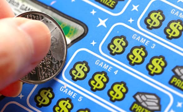 A lottery scratch game with someone holding a coin preparing to scratch off the film.