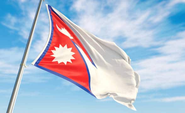 Nepalese national flag flying on a pole against the blue skies.