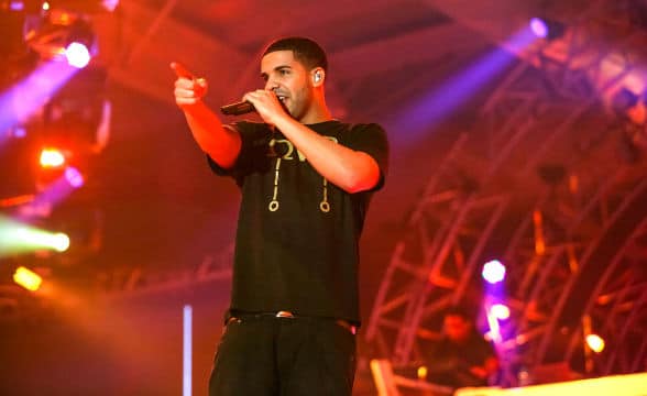 Rapper Drake performing on stage, holding the mic and pointing a finger at someone or something back in the crowd.