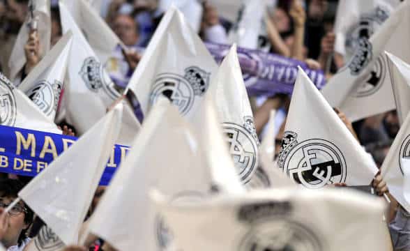 Real Madrid fans holding and waving team paraphernelia.