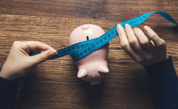 A person measuring a piggy bank with a tape.