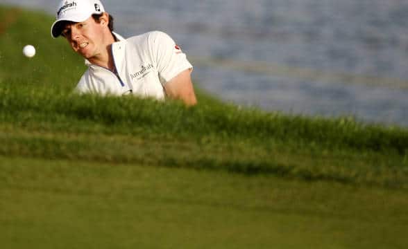 A photo of Rory McIlroy taking a swing at a ball shot with just the golfer's upper body in the photo and the ball seen flying away.