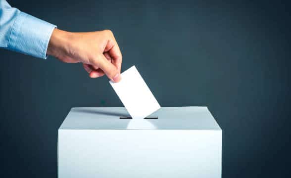 A hand putting a vote in a ballot box.