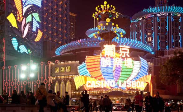 Casino Lisboa in Macau, China with bucnh of people sitting outside on benches and walking around at night.