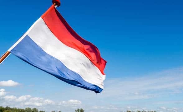 The Dutch national flag flying against blue skies.