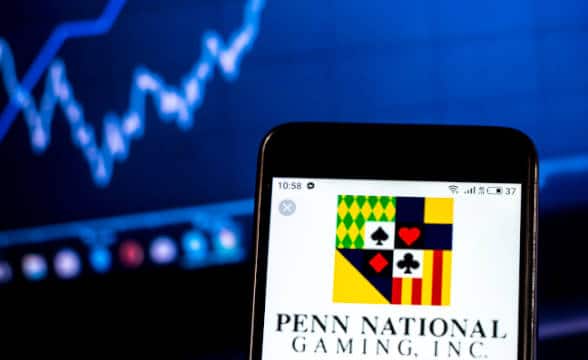 A Penn National Gaming logo loaded on a smartphone against a background trading stocks.