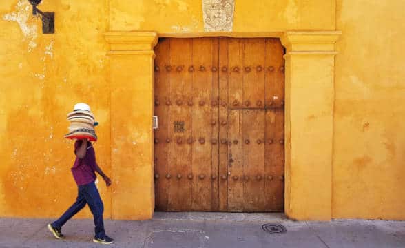 A person walking with something on their shoulder in Colombia against a yellow house background.