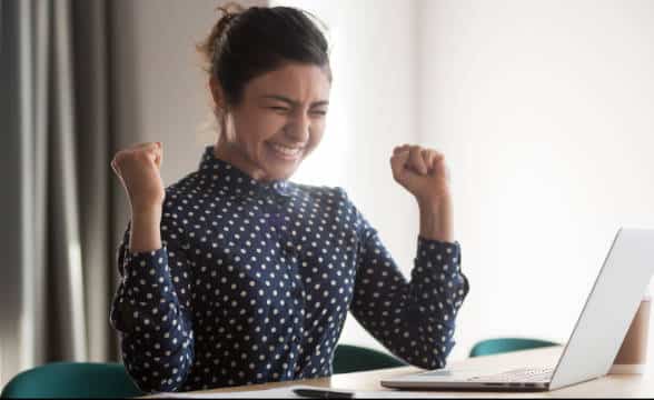 A lady is cheering in front of her computer after winning a reward.