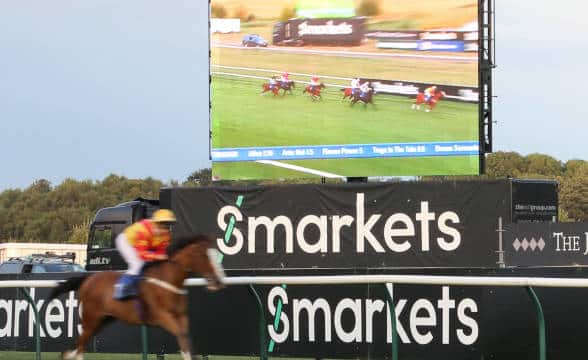 A horse race in progress with the Smarkets logo and signage on the periphery of the race track.