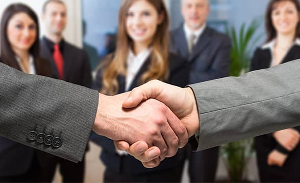 Two men shake hands in front of other businesspeople