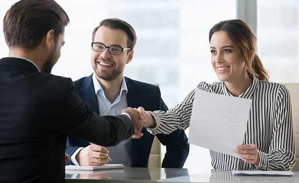 A person is welcomed to a company by two businesspeople