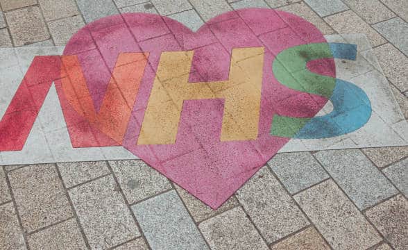 The NHS logo in colors on a pavement.