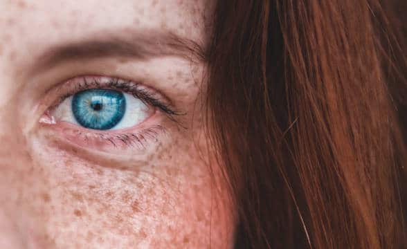 A red-haired freckled woman's face with blue eyes.