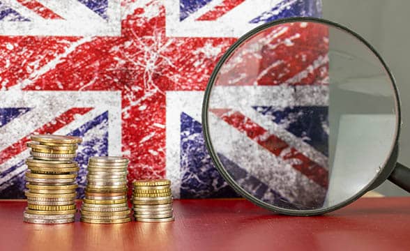 A magnifying glass in front of the British flag and a pile of coins