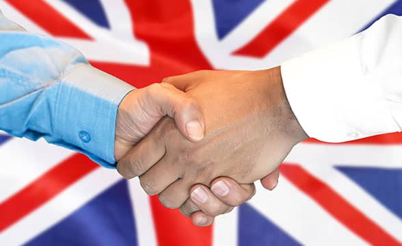 Two people shake hands before the UK flag