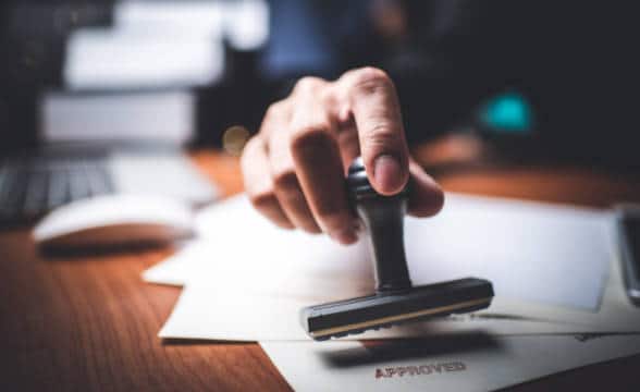 Close up photo of a person placing stamp Approved on documents