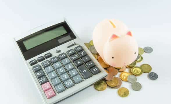 A piggybank on a bunch of coins next to a calculator.