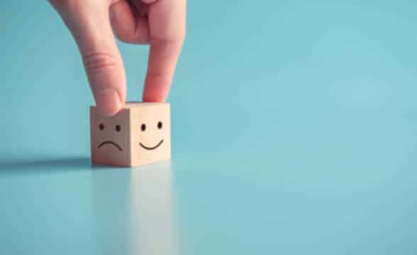 Close up photo of a hand holding a cube with smiley and sad face