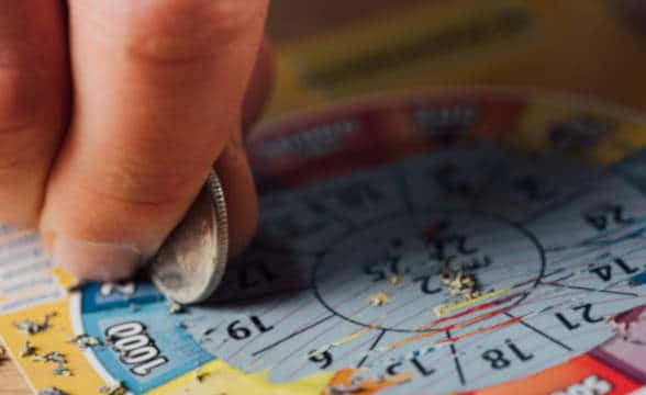 A photo of a person scratching off ticket with a coin