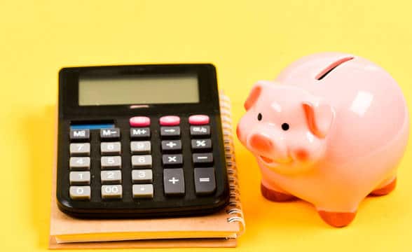 A piggybank sitting next to a calculator against a yellow background.