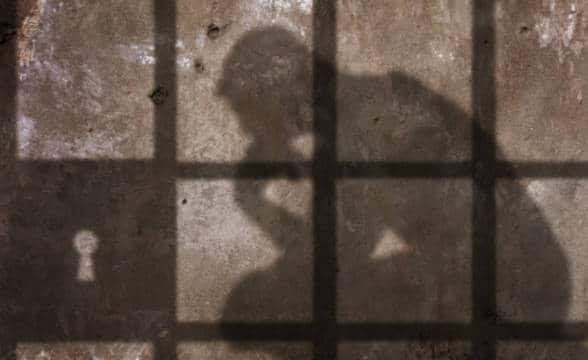 A shadow of a thinking man behind jail bars