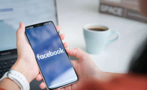 Close up photo of a woman holding a smartphone with a Facebook app