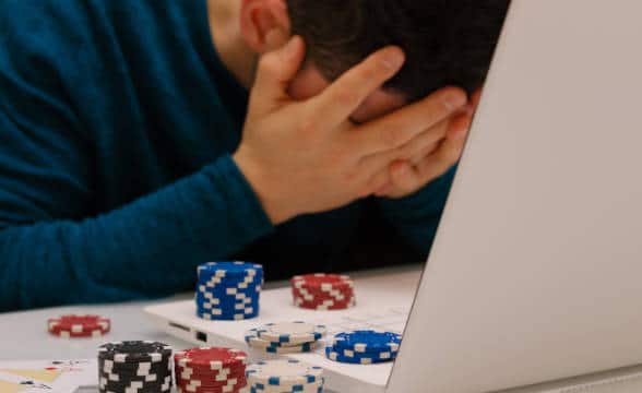 A troubled gambler holding his head in front of a laptop