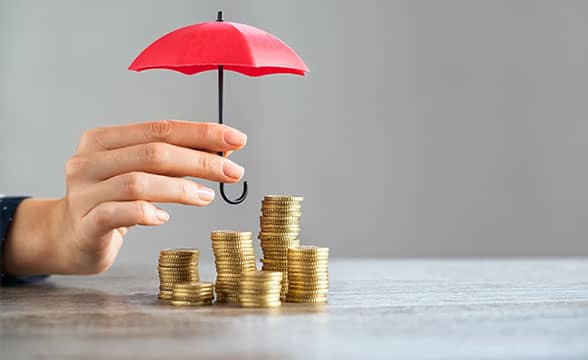 A hand holds a little umbrella over stacks of coins