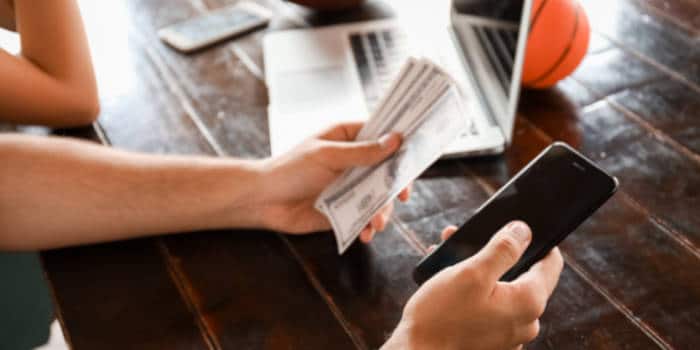 Close up photo of a young man holding money and a smartphone