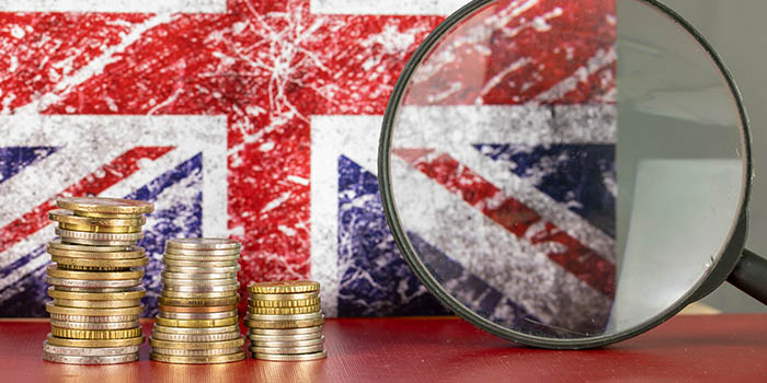 A magnifying glass in front of the British flag and a pile of coins