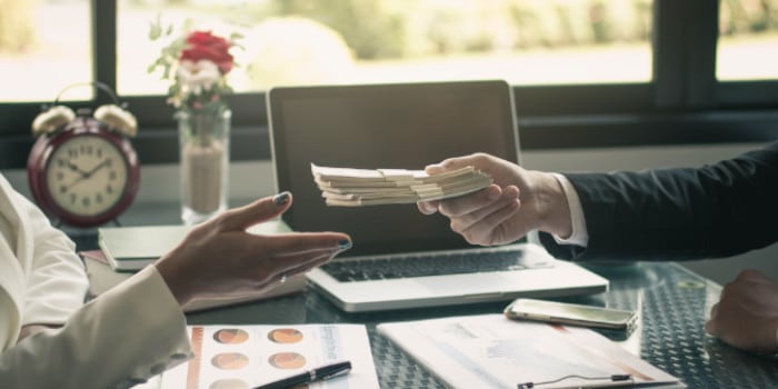 Close up photo of the hand of a man giving stacks of money to a businesswoman