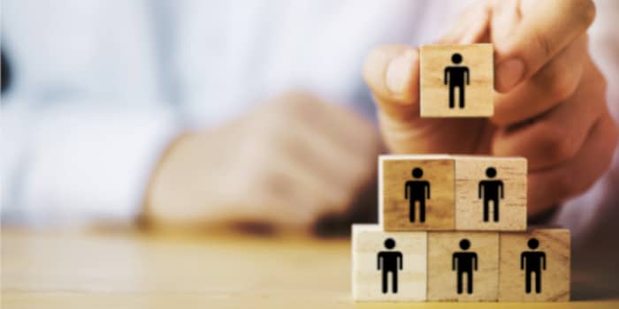 A businessman stacking wooden cubes with human icons, building a pyramid