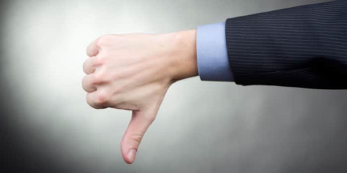 A close up photo of the hand of a businessman making a thumb down gesture, symbol for rejection