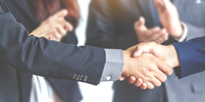 Two businessmen shaking hands and people clapping in the background