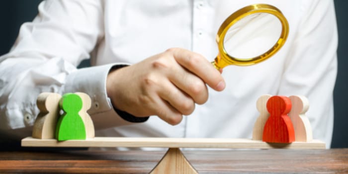 Man looking through magnifying glass at figures on a scale