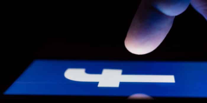 Finger tapping on the screen of a smartphone with open Facebook app