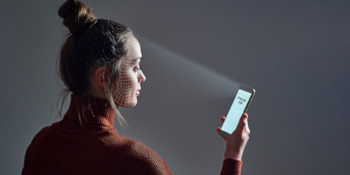 A woman holding a smartphone unlocking it via face ID, facial recognition