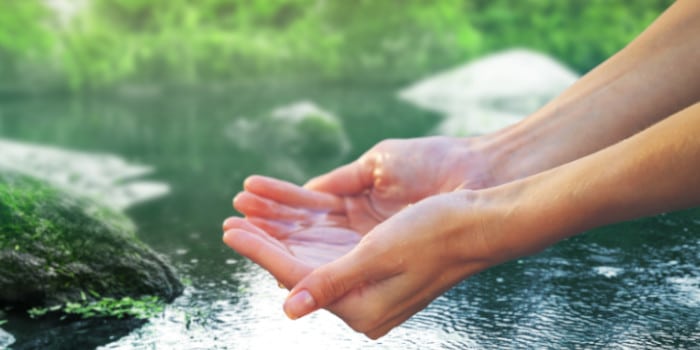 Hands of a woman holding water in her hands from a natural spring